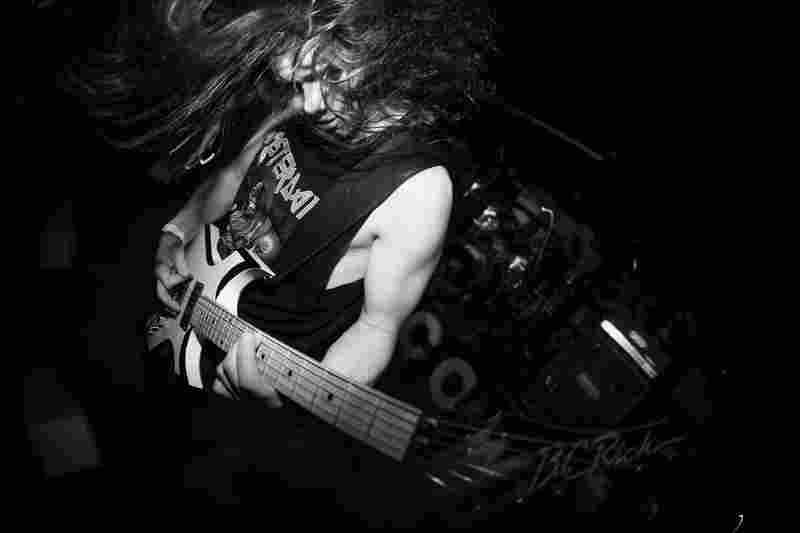 Black-and-white photograph of a guitarist performing at a live metal show.